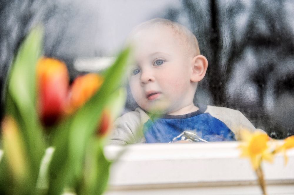 a young boy looking out a window at flowers