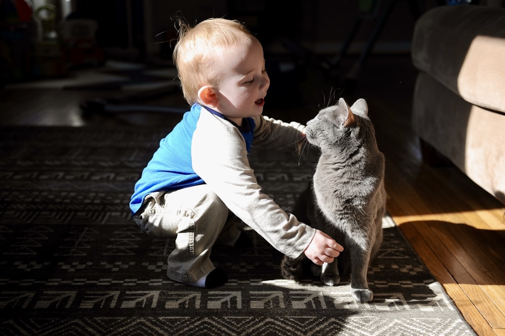 a baby playing with a cat on the floor