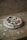 A rustic-style pizza with a slightly irregular shape sits on a wooden board. The pizza is topped with tomato sauce, fresh basil leaves, and mozzarella cheese. The background consists of a textured, unfinished plywood surface.