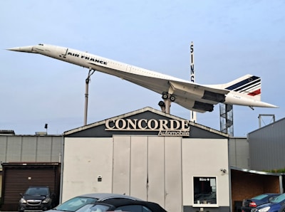 A Concorde jet in Air France livery is displayed on a rooftop at an automobile business named Concorde. The aircraft is mounted as if taking off, showcased on a tall stand. Multiple cars are parked in front of the building.
