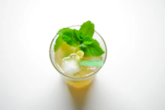 A vibrant glass of mango shake topped with fresh mint leaves and a straw.