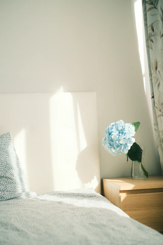 A serene bedroom scene bathed in soft blue and purple hues, featuring a cozy bed with plush pillows and a glowing white noise machine on the nightstand.