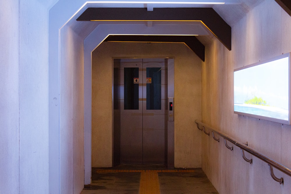 a long hallway with a metal door and a flat screen tv on the wall