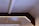 A geometric ceiling design with beams and integrated lighting. The ceiling features a rectangular frame with embedded strip lights, providing a soft, ambient glow. The materials used appear to be a combination of concrete and wood or metal, creating a modern, industrial look.