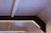 A geometric ceiling design with beams and integrated lighting. The ceiling features a rectangular frame with embedded strip lights, providing a soft, ambient glow. The materials used appear to be a combination of concrete and wood or metal, creating a modern, industrial look.