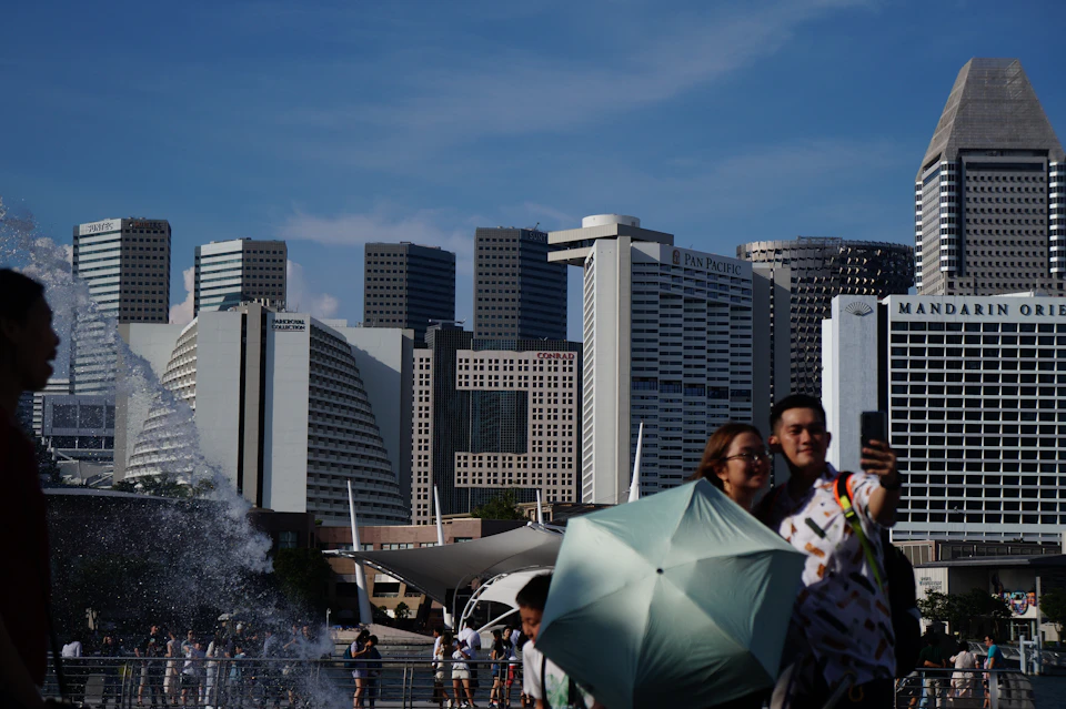 People sheltering under umbrellas in front of the Singapore city skyline during a monsoon downpour