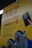 A yellow poster with instructions in English and Chinese about taking out a card and tapping it at a terminal, accompanied by an illustration of a hand holding a card and tapping it against a card reader. The poster also features illustrated turnstiles.