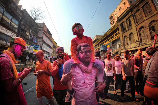 Crowd celebrating Holi with colorful powders flying under sunny skies at the Holifest Bangalore event.