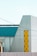 A modern industrial building featuring geometric shapes and a mix of materials. The structure has metal siding with a prominent yellow accent section in a zigzag pattern. The facade includes teal and grey panels, and there are several horizontal and vertical lines creating a minimalist architectural aesthetic.