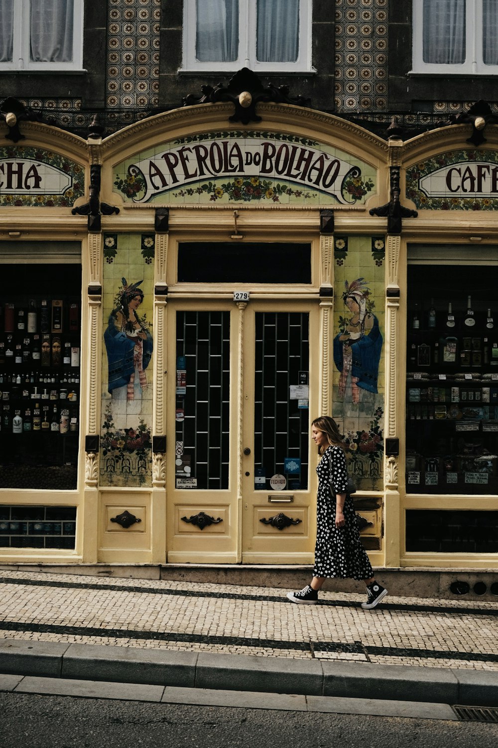 a woman walking down a street past a store front