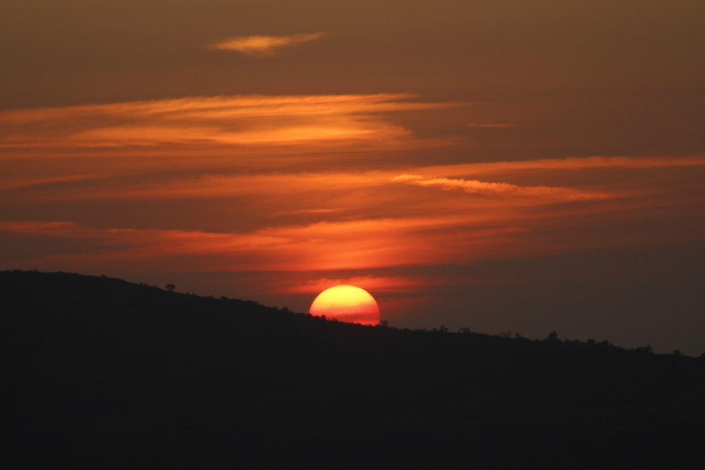 the sun is setting over a hill with trees