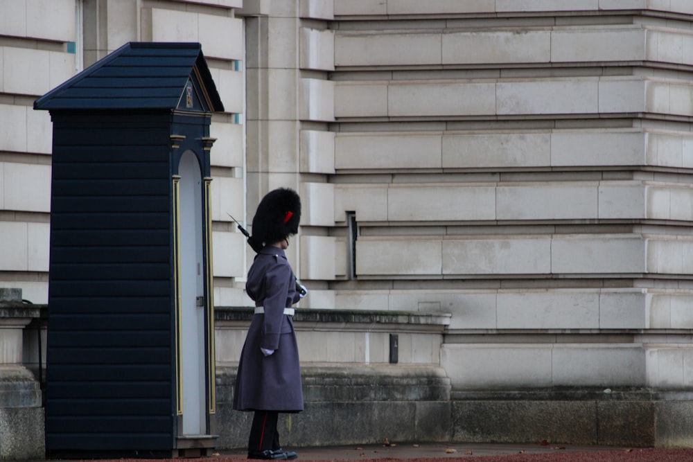 una persona in un cappotto e un cappello in piedi di fronte a un edificio