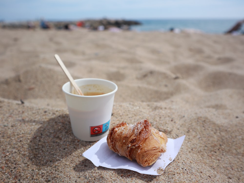 a cup of coffee and a croissant on a beach