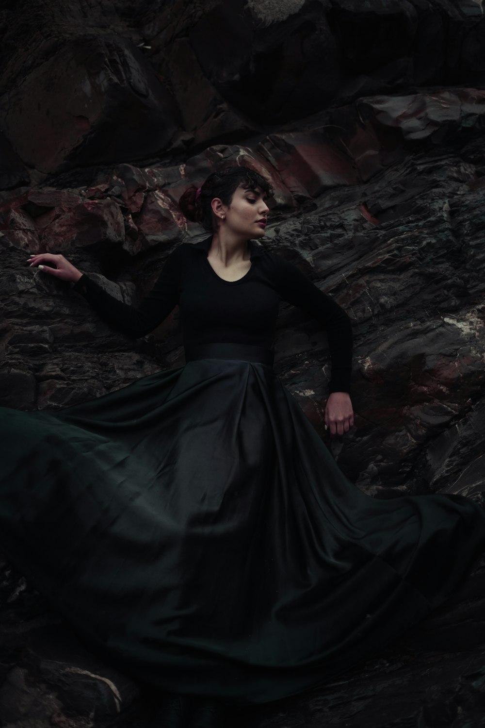 a woman in a long black dress standing on rocks