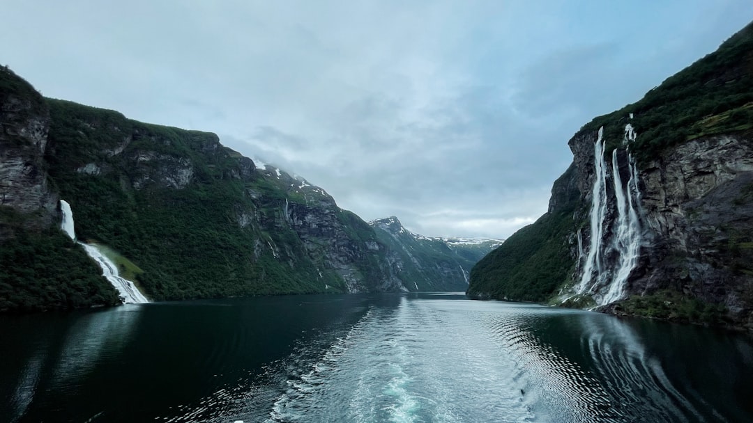 a body of water surrounded by mountains and a waterfall, Breathtaking view of Geirangerfjord and Seven Sisters waterfall
