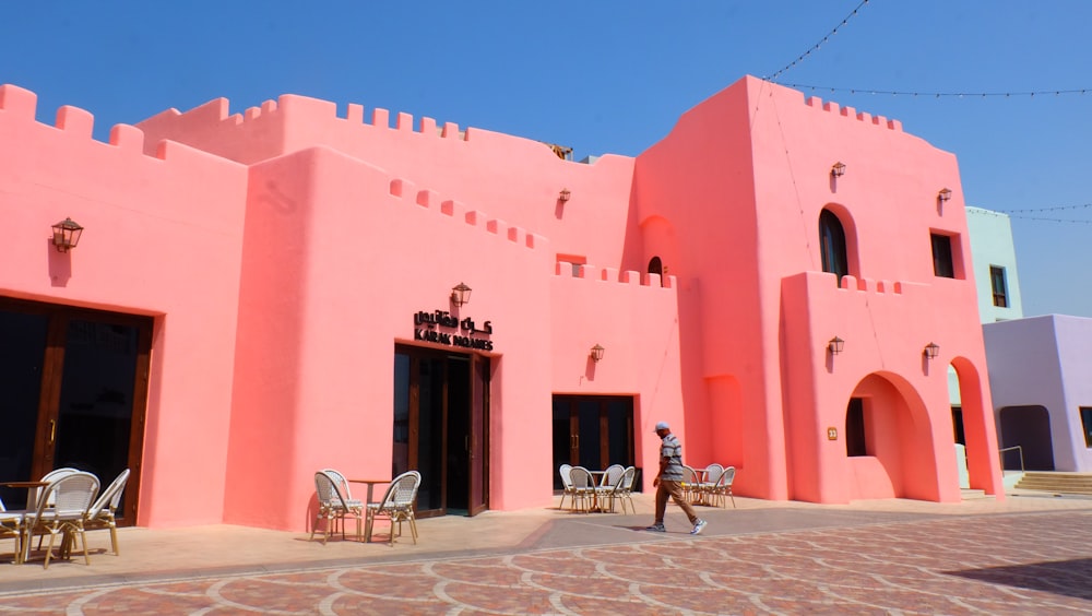 a large pink building with tables and chairs in front of it