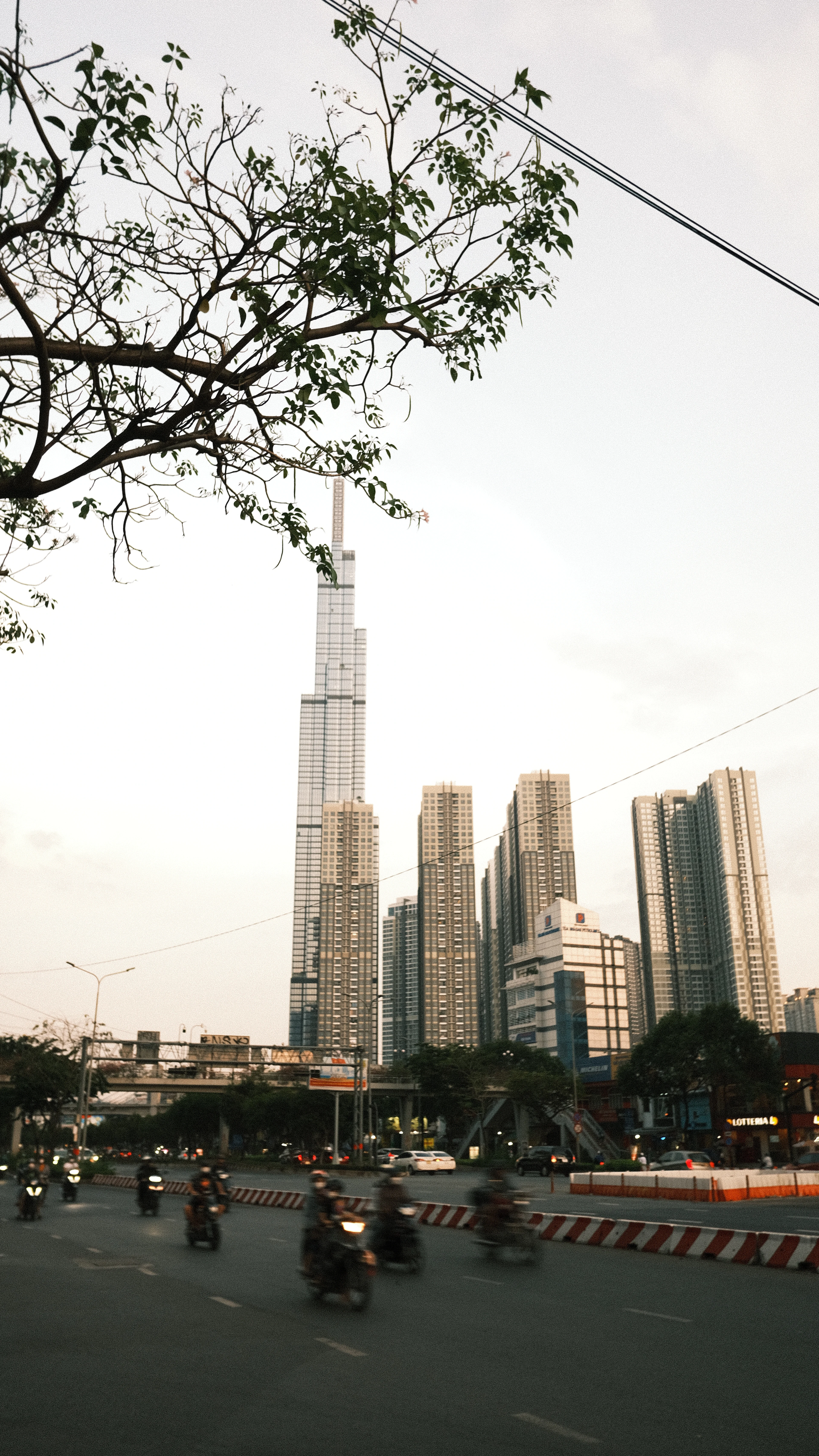 Landmark 81 tower glows above a Ho Chi Minh City street at dusk as motorbikes pass below.