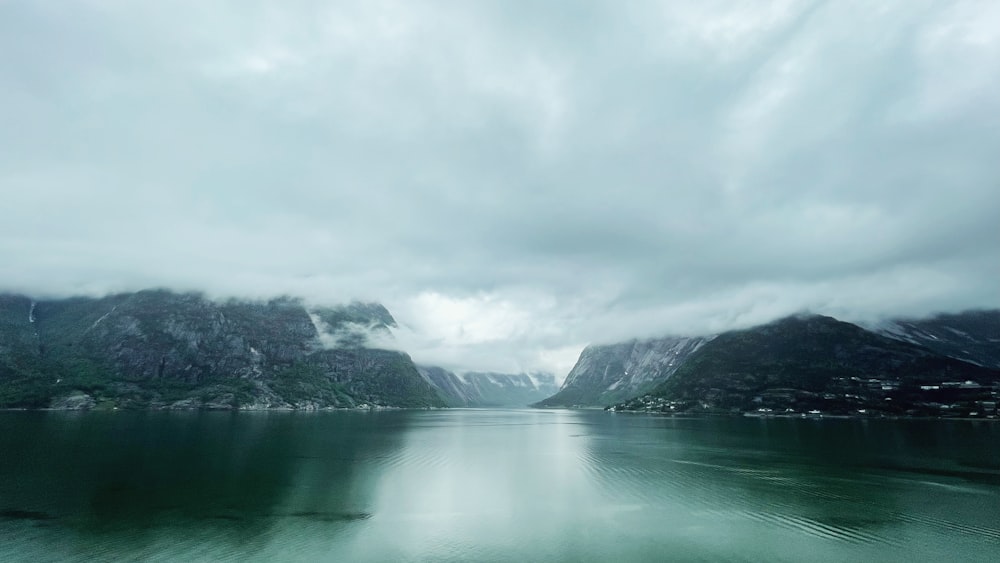 a body of water surrounded by mountains under a cloudy sky