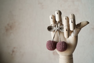 a wooden hand with two knitted balls hanging from it