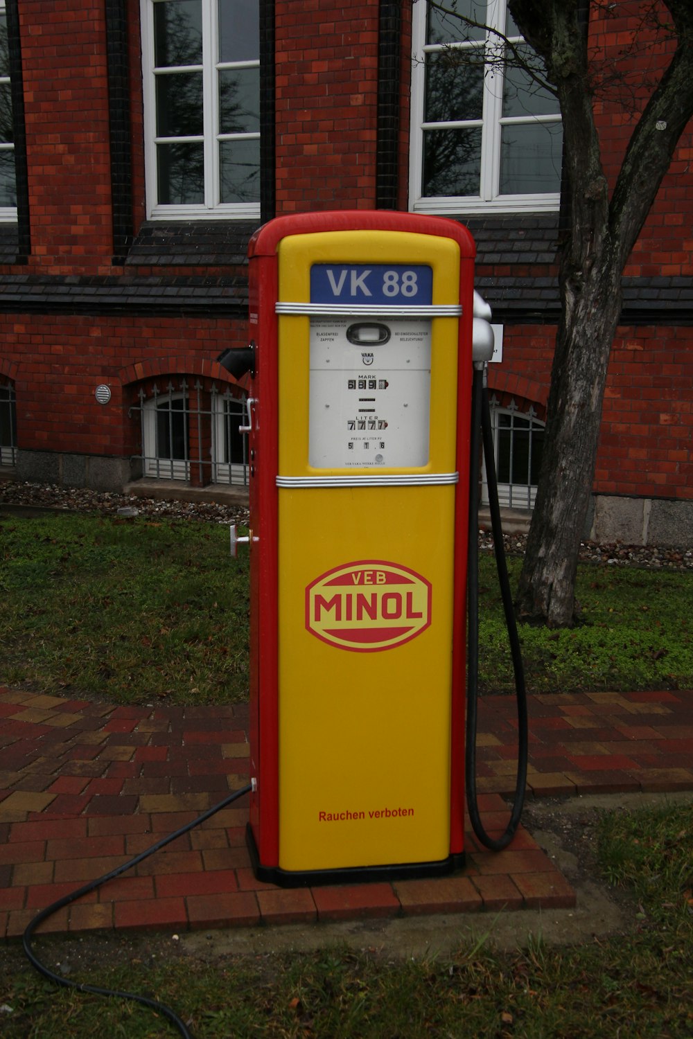 a yellow and red gas pump sitting in front of a brick building