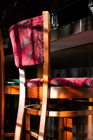 A sleek wooden bar stool with a curved seat and metal footrest set against a cozy kitchen backdrop.