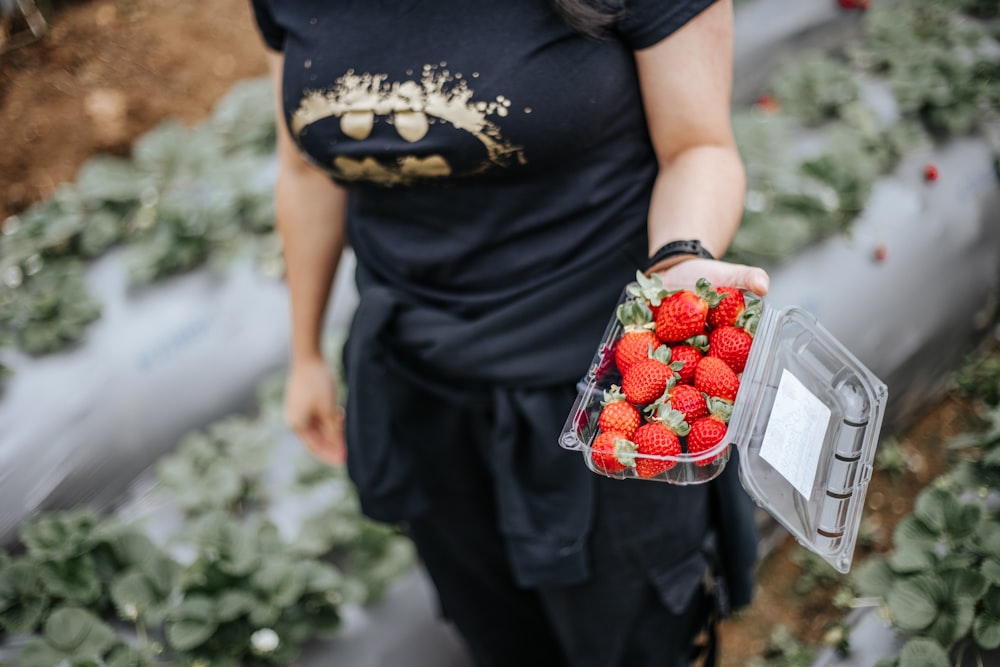 a woman holding a plastic container full of strawberries