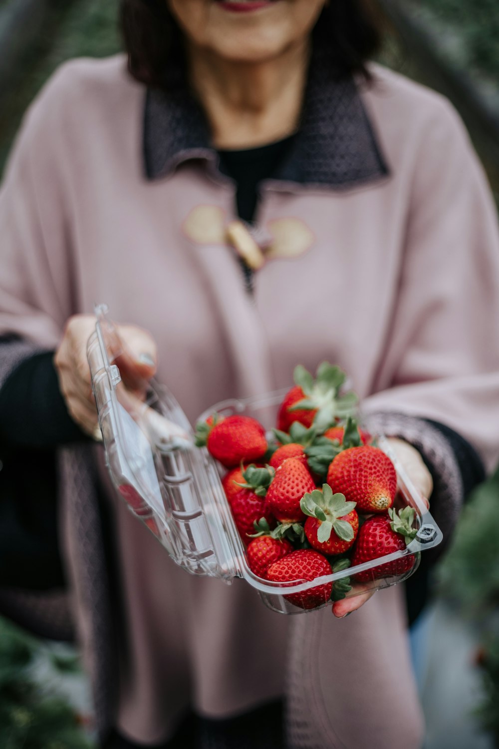 a woman holding a plastic container full of strawberries
