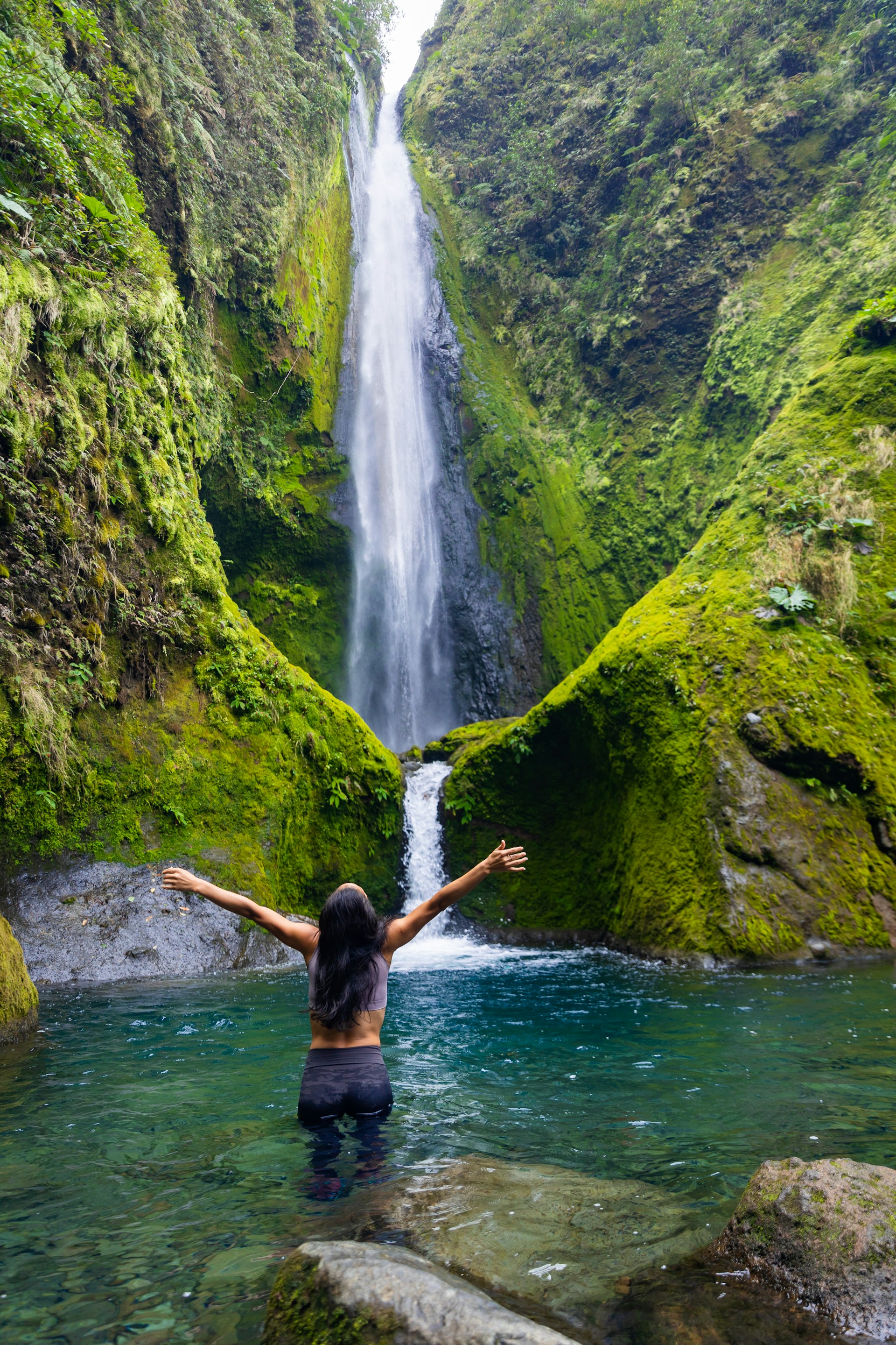 a woman standing in the water in front of a waterfall