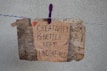 A handmade sign with the message 'Creativity is better left unconfined' is attached to a weathered, textured background using a purple clothespin on a blue and white rope. The sign blends an artistic mix of handwritten styles in a combination of black and some colorful accents.