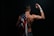 A muscular person with a rugged, athletic appearance is seen from behind, draped in a US flag. Their right arm is bent, with a taped wrist and hand, suggesting they've been engaged in intense physical activity. The skin is marked with dirt or bruises, conveying a sense of struggle or endurance.