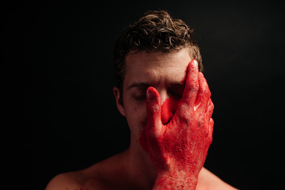 a man covered in red paint covering his face