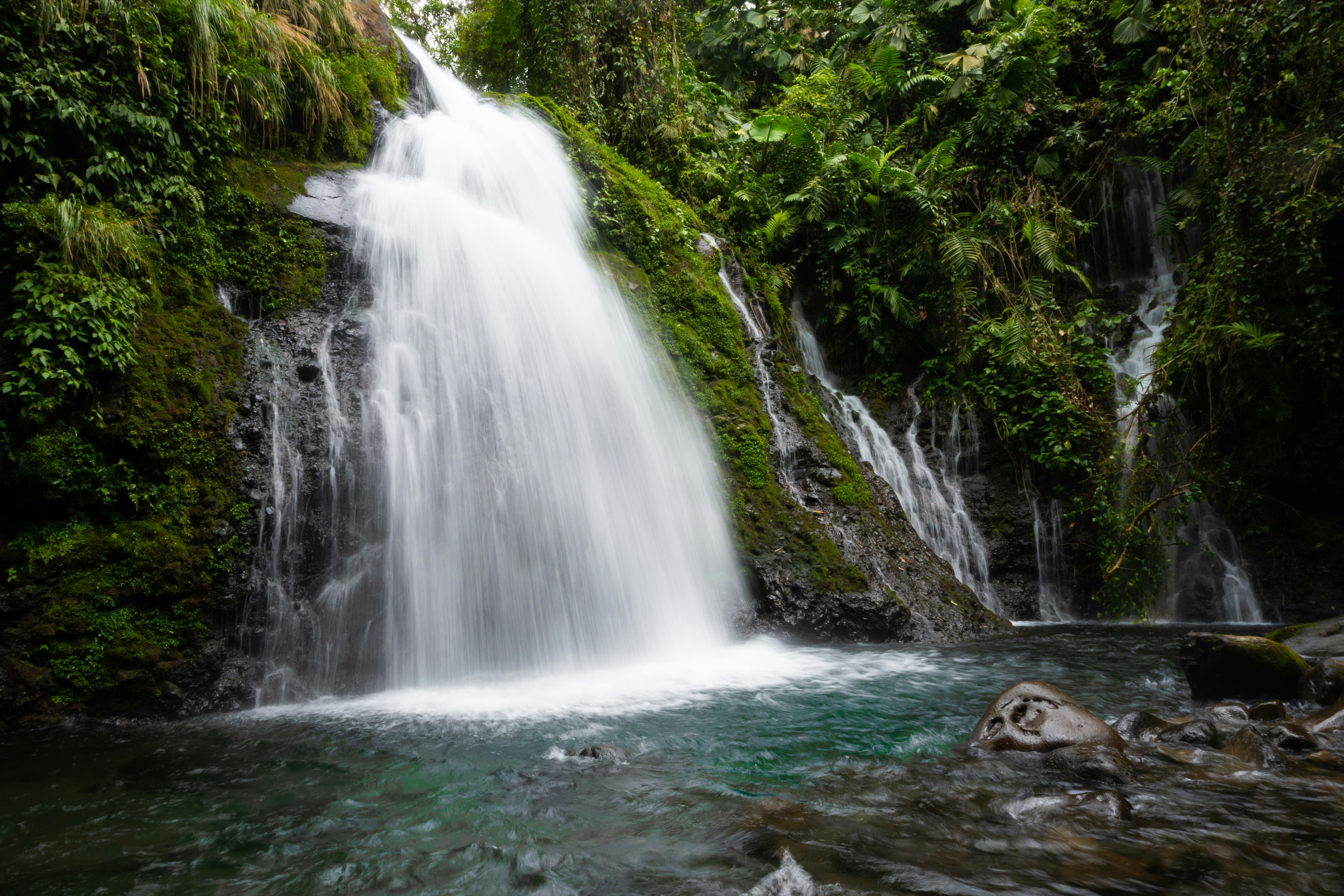 a large waterfall in the middle of a forest, Emerald Falls - A small waterfall is surrounded by lush greenery, casting a beautiful emerald hue on the water in Costa Rica.