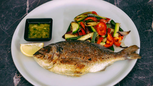 A vibrant plate of attiéké with grilled fish, garnished with fresh vegetables and spicy sauce.