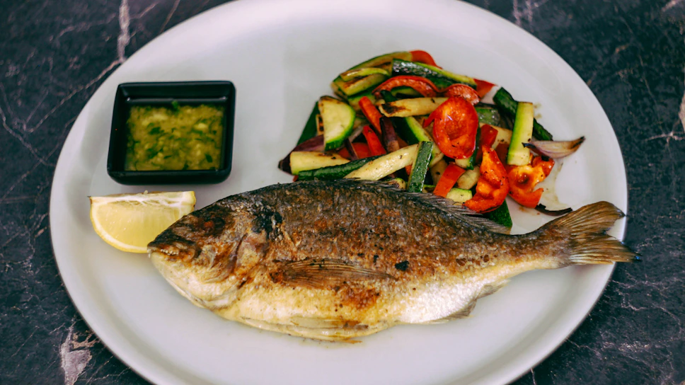 A vibrant plate of freshly grilled Mediterranean fish served with colorful vegetables by the riverside at Nehirbahçe.