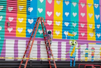 a man on a ladder painting a mural on the side of a building