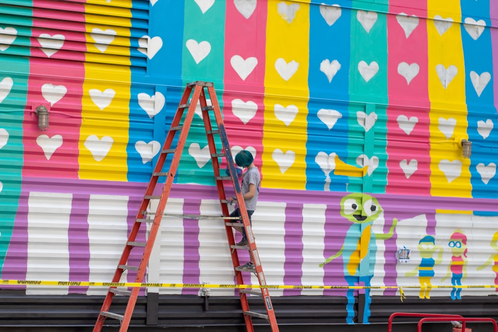 a man on a ladder painting a mural on the side of a building