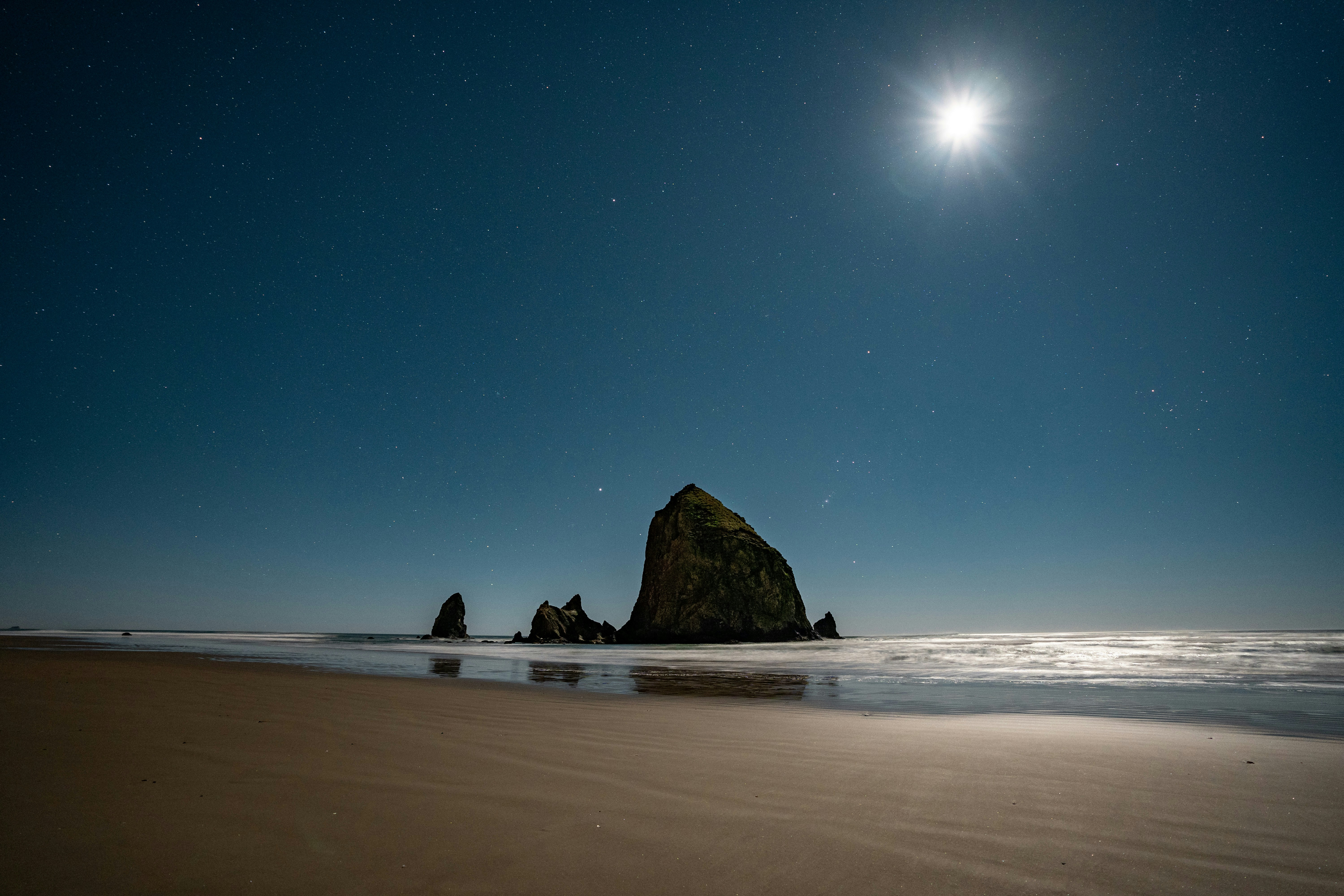 Une pleine lune brille sur une formation rocheuse sur la plage