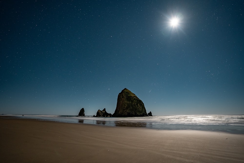 a full moon shines over a rock formation on the beach