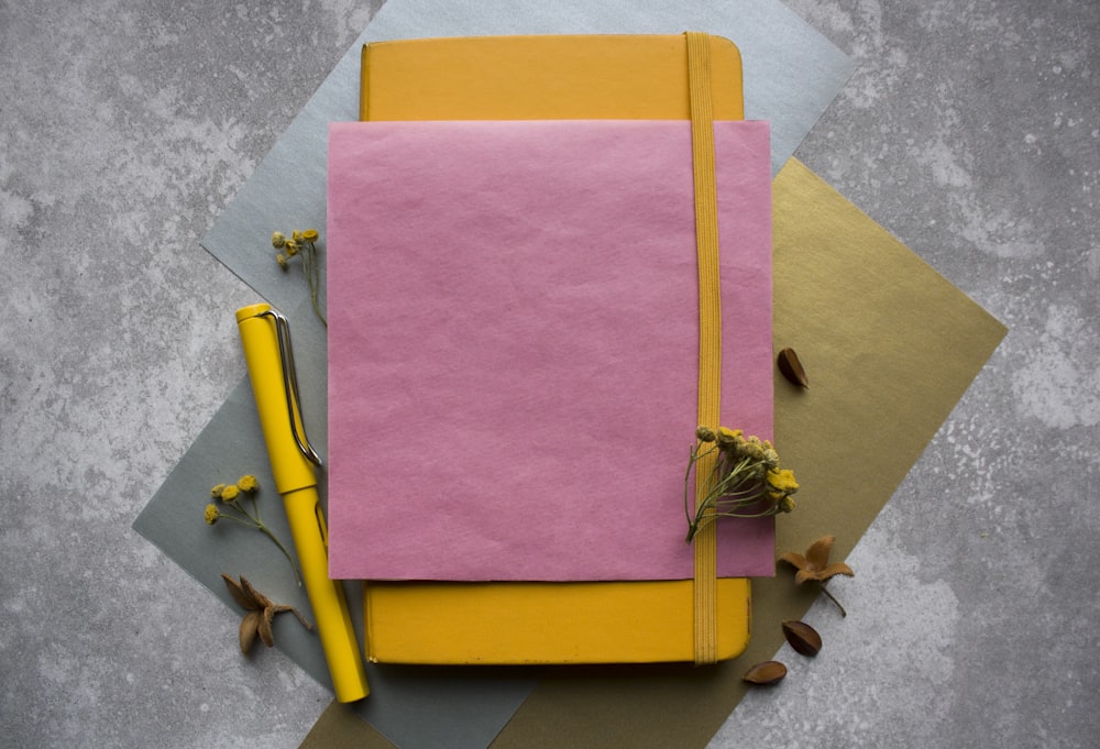 a pink and yellow notebook with a pen on top of it