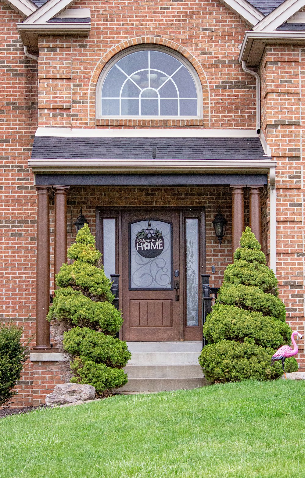 a front door of a brick house with two evergreen trees