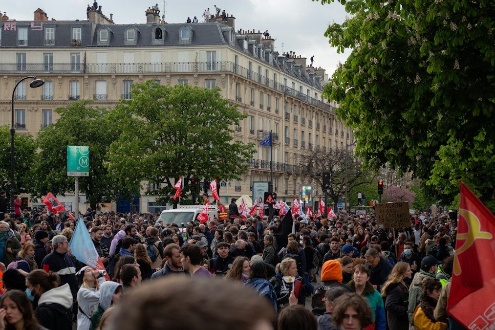 Une foule de manifestants avec drapeaux et pancartes sur un boulevard parisien bordé d’immeubles haussmanniens