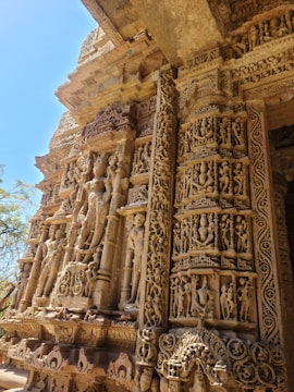 Intricate stone carvings adorn a historical temple facade, showcasing detailed sculptures of human figures and ornamental patterns. The craftsmanship captures a rich cultural heritage, with statues and reliefs in various poses set against a backdrop of textured stone.