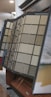 An assortment of carpet samples displayed on a standing rack, featuring various textures and colors including beige, blue, and gray. The setup is indoors, likely in a showroom or retail store, with a focus on home decor options.
