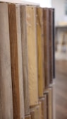 Several wooden planks are arranged vertically in a row, showcasing various shades and textures of wood. The focus is on the left side, with the planks gradually fading into the background on the right.