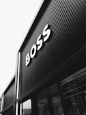 A black and white photograph of a building with large signage displaying the word 'BOSS' in bold letters. The architecture features vertical lines that create a modern and sleek appearance.