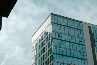 A detailed exterior shot of a commercial office building with reflective glass windows capturing the sky and nearby urban environment.