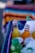 Several colorful bottled drinks are partially submerged in crushed ice inside a cooler, with vibrant stripes of a textile in the background.