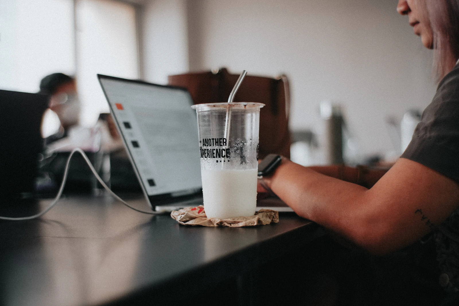 A person typing on a laptop at a cafe table next to an iced drink