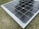 A solar panel resting on a grass surface with visible grass blades surrounding the panel. The solar panel has a grid of black photovoltaic cells separated by white lines.