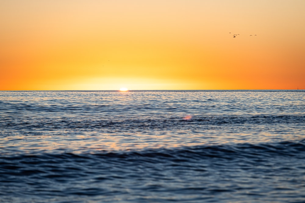 the sun is setting over the ocean with a boat in the distance